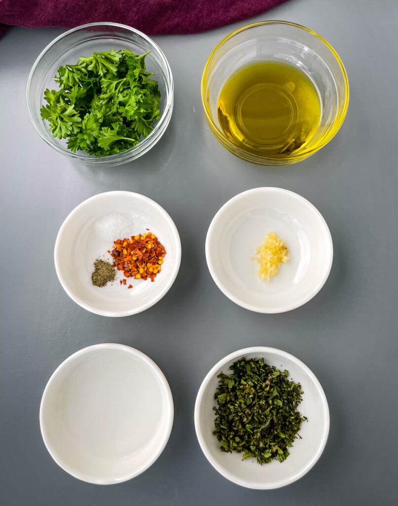 fresh parsley, fresh oregano, olive oil, garlic, vinegar, and crushed red pepper in separate bowls.