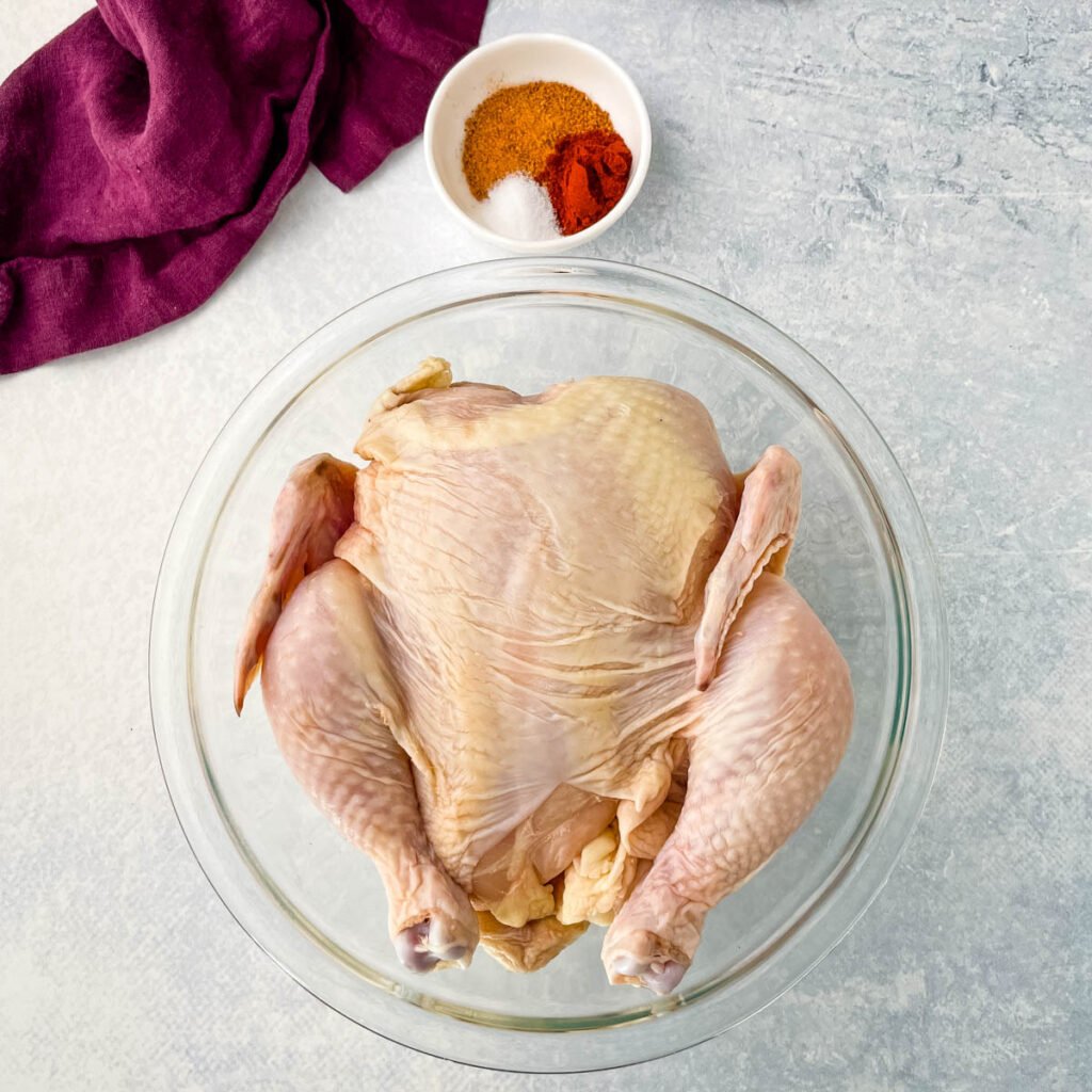 raw whole chicken in a glass bowl and a bowl of seasonings