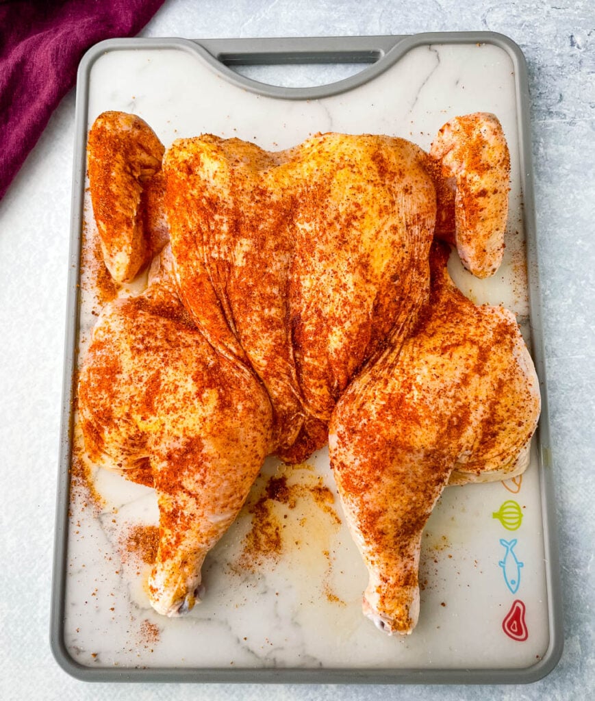 raw seasoned spatchcock chicken on a cutting board