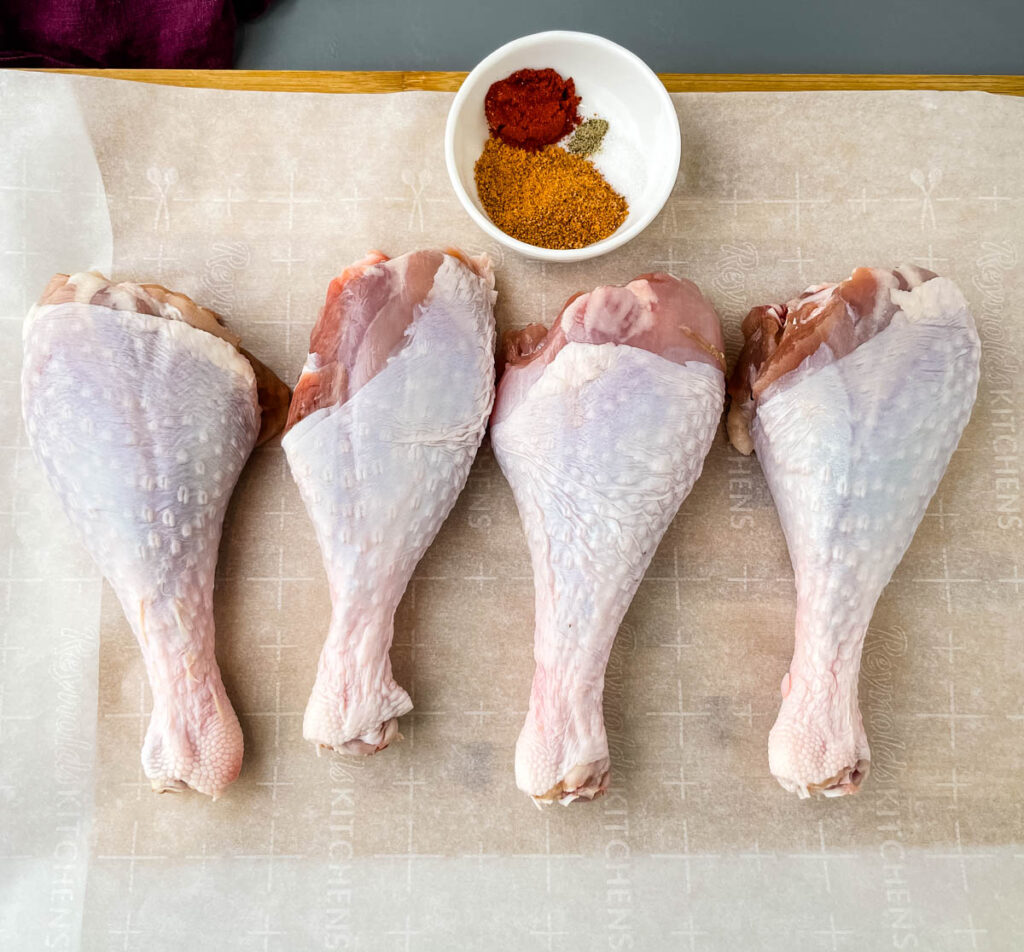 raw turkey legs on parchment paper with a bowl of seasonings