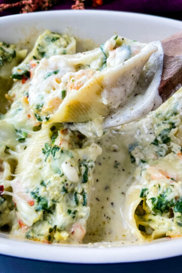a wooden spoon holding seafood lobster, shrimp, and crab stuffed shells in a baking dish