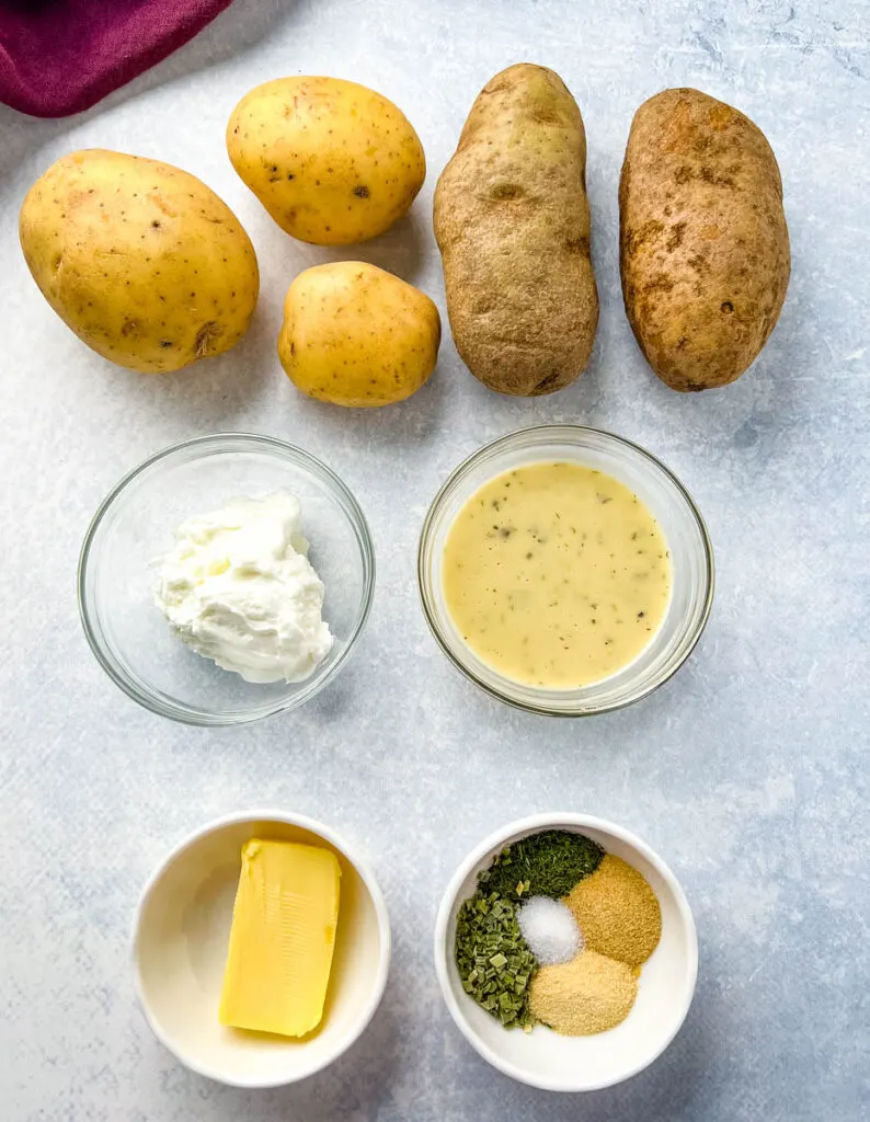 Yukon gold and russet potatoes on a flat surface with plain Greek yogurt, ranch dressing, ranch seasoning, and butter in separate bowls