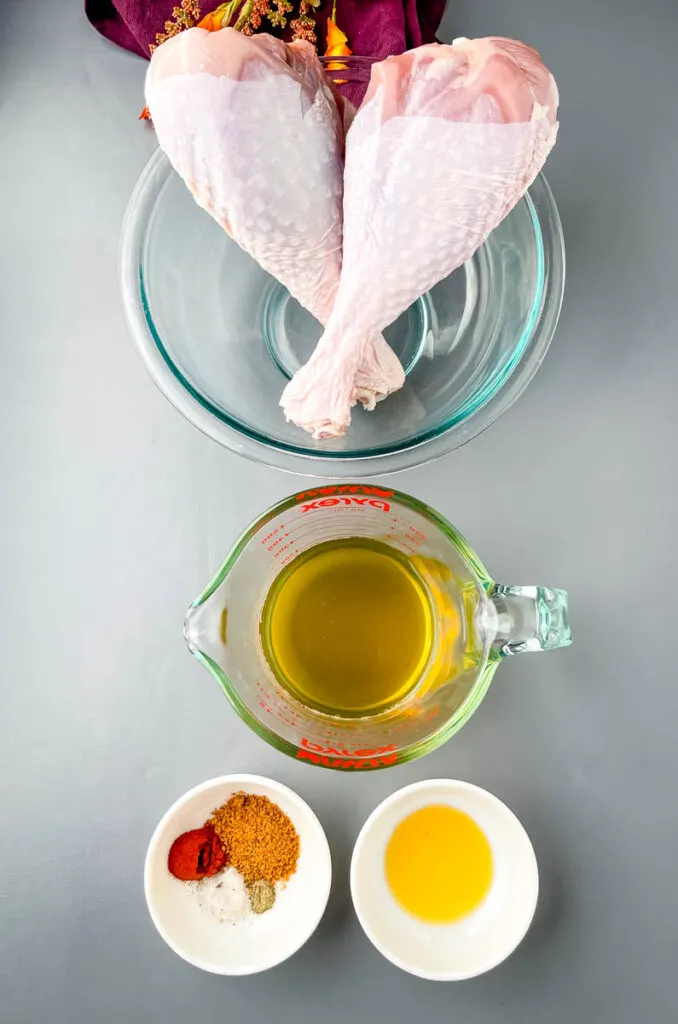 2 raw turkey legs, chicken broth, and spices in separate bowls