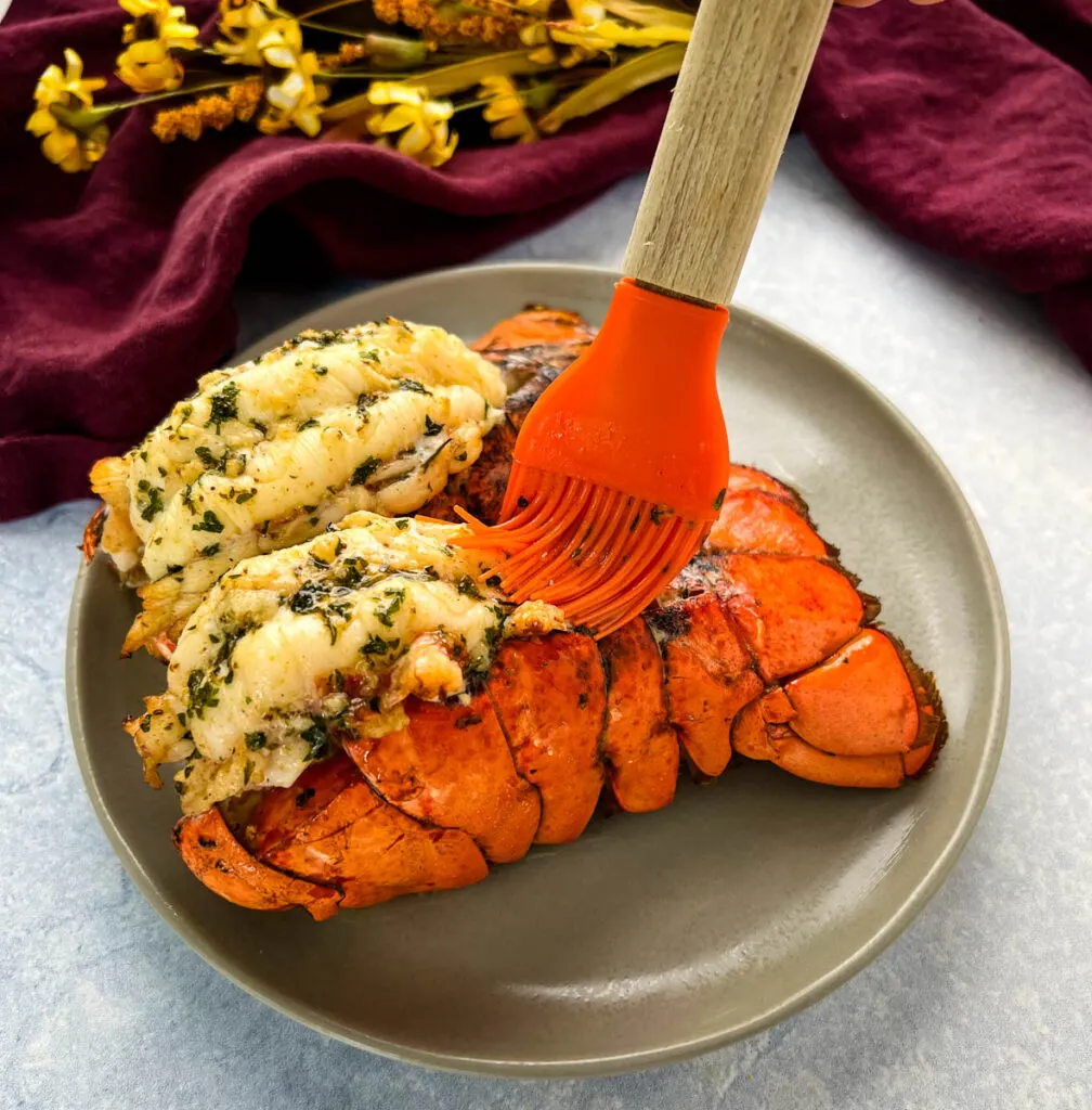 air fryer lobster tails on a white plate being drizzled with butter