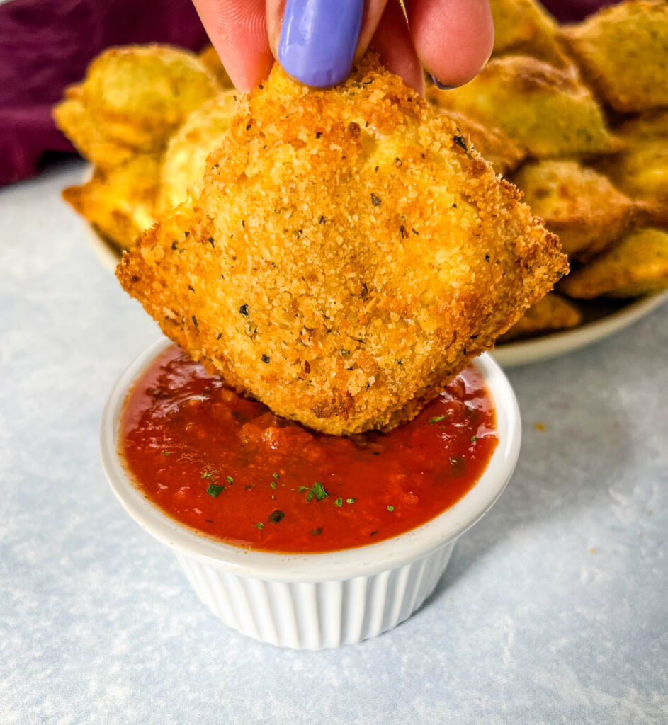 person holding air fryer toasted fried ravioli with marinara sauce