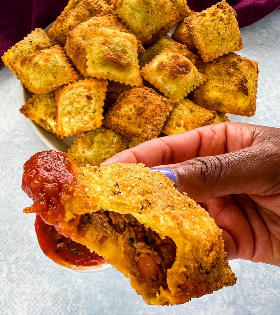 person holding air fryer toasted fried ravioli with marinara sauce