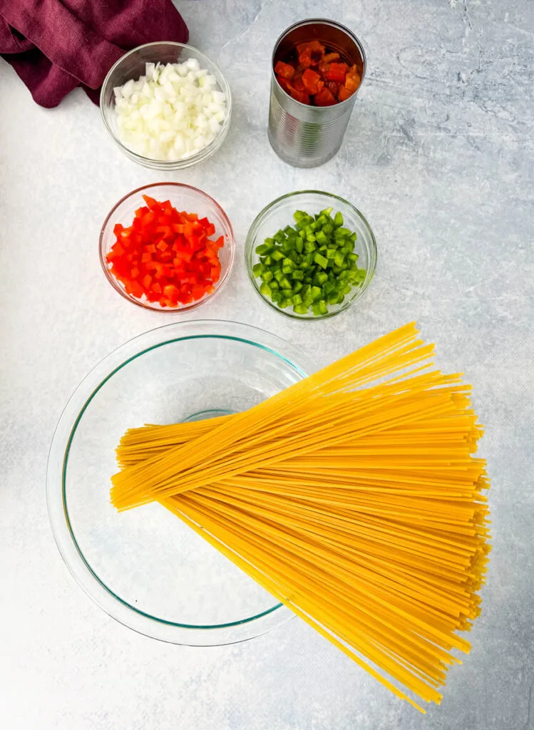 dry spaghetti pasta, raw red peppers, green peppers, onions, fire roasted tomatoes on a flat surface