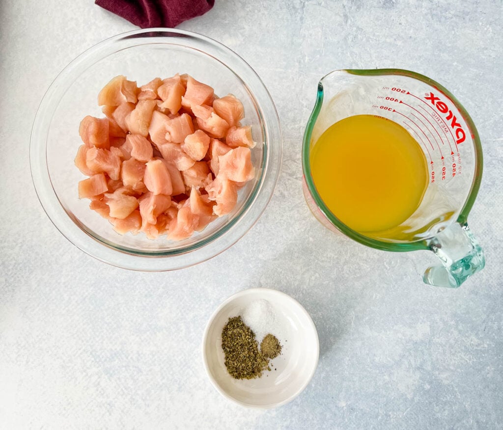 raw chicken breast cut into chunks, chicken broth, and spices in separate bowls