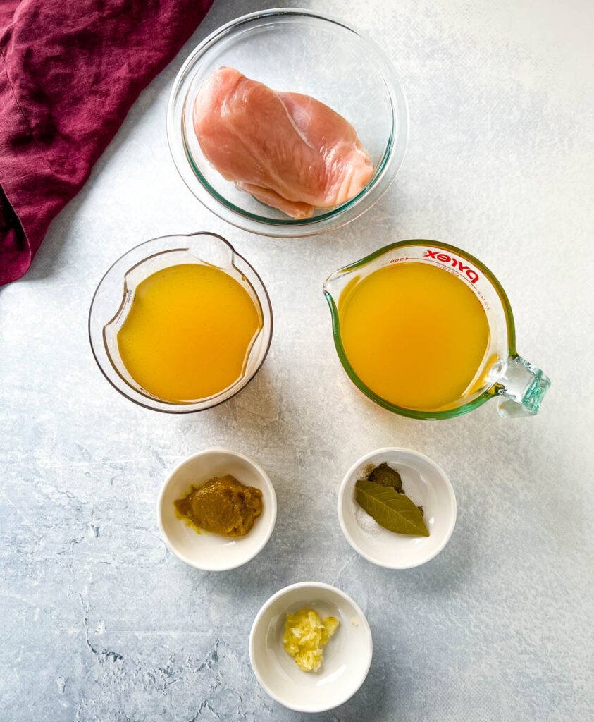 raw skinless chicken breasts, broth, and spices in separate bowls
