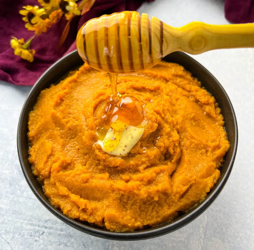 mashed sweet potatoes in a bowl with butter and brown sugar being drizzled in honey