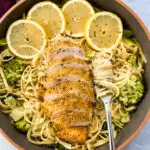 lemon chicken pasta in a pan with fresh lemons, spinach, and broccoli