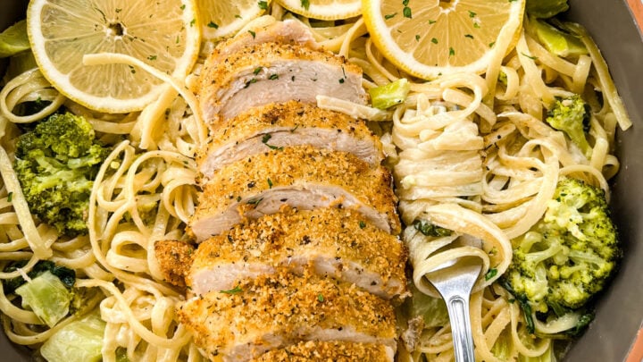 lemon chicken pasta in a pan with fresh lemons, spinach, and broccoli