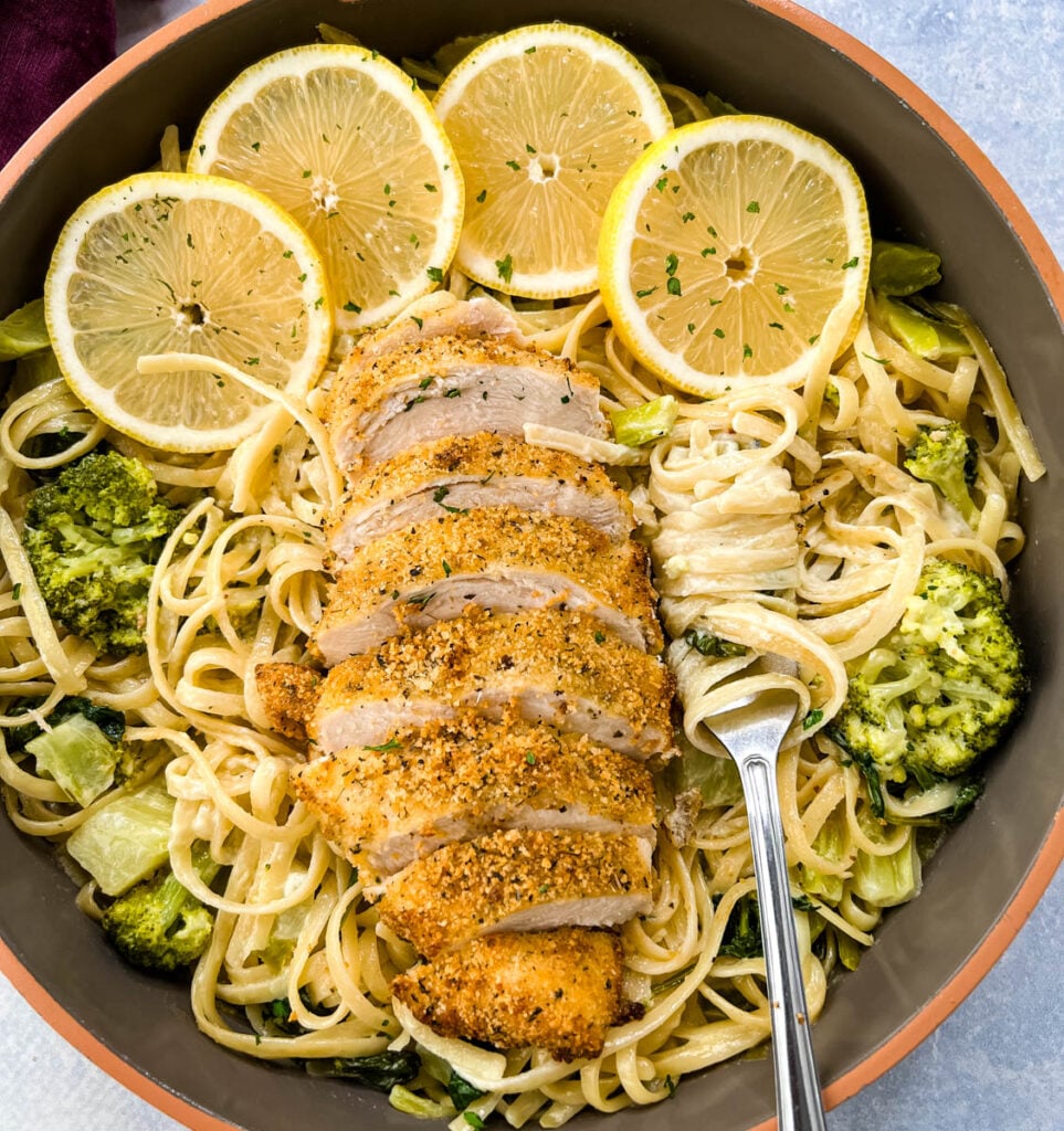 lemon chicken pasta in a pan with fresh lemons, spinach, and broccoli