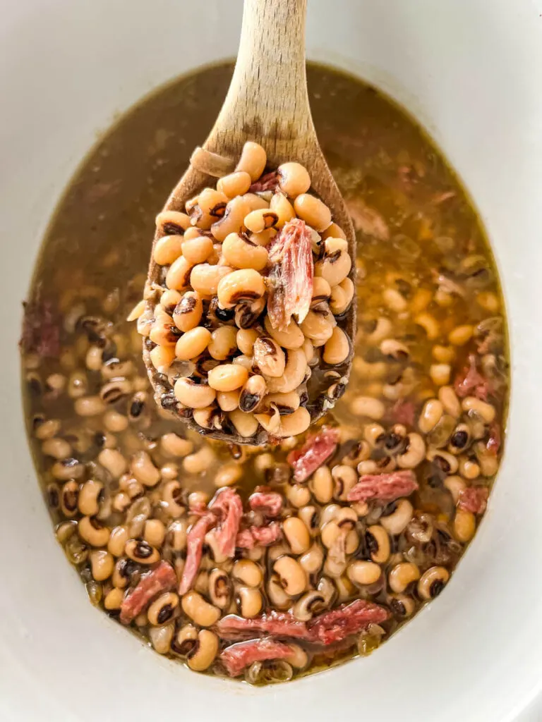 a wooden spoonful of cooked black eyed peas in slow cooker Crockpot