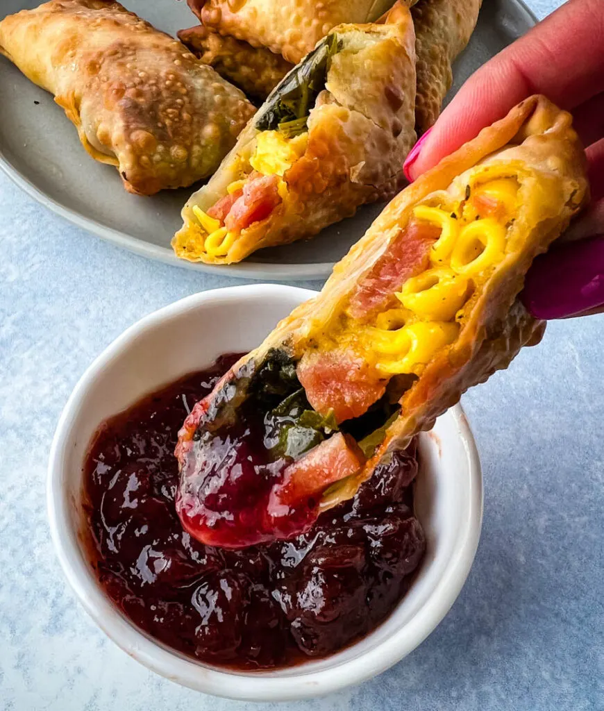 person holding Thanksgiving soul food egg roll and dipping it in cranberry sauce