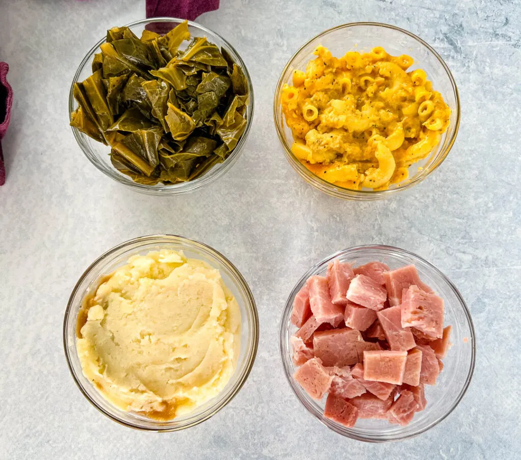 collard greens, mac and cheese, mashed potatoes, and chopped ham in separate bowls