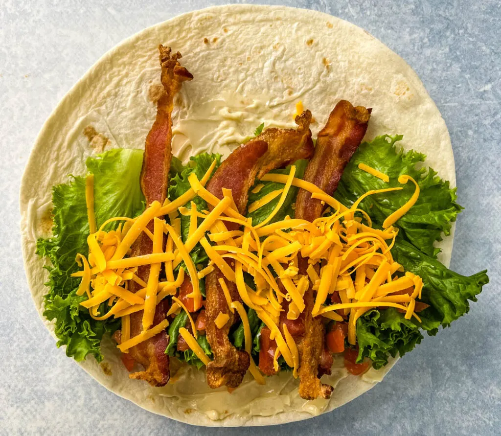blt wrap with bacon, lettuce, tomato, and mayo on a plate in a tortilla
