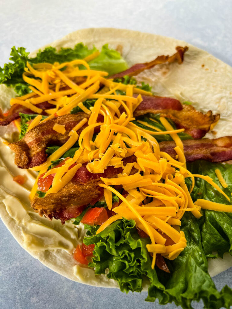 blt wrap with bacon, lettuce, tomato, and mayo on a plate in a tortilla