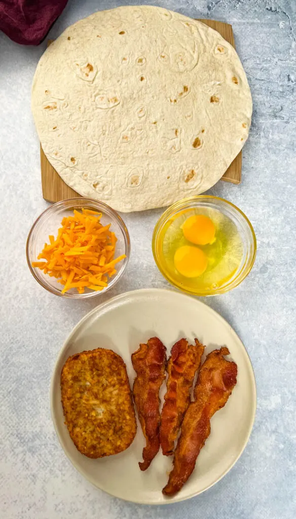 tortilla, eggs, shredded cheese, bacon, and hashbrowns on separate plates