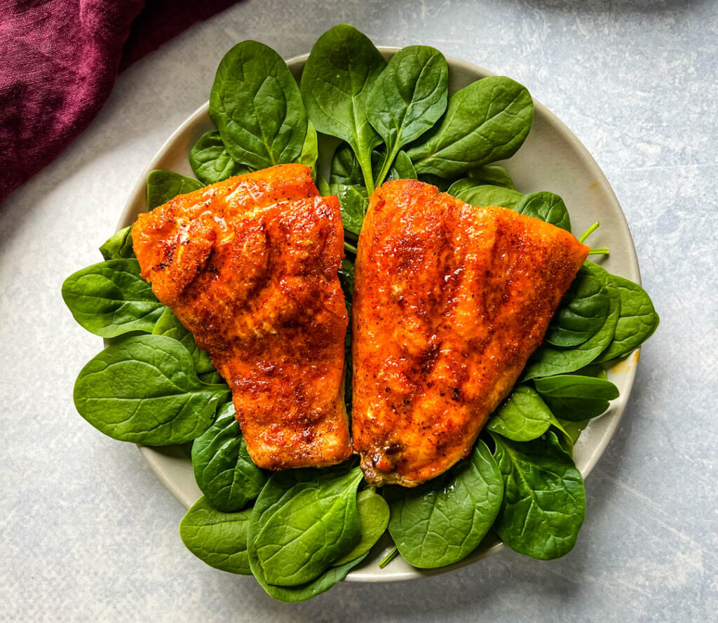 cooked indoor grilled salmon on a plate with fresh spinach