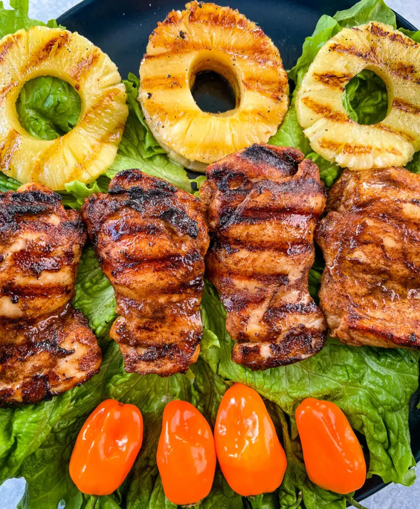 Jamaican jerk chicken thighs on a plate with peppers and grilled pineapples