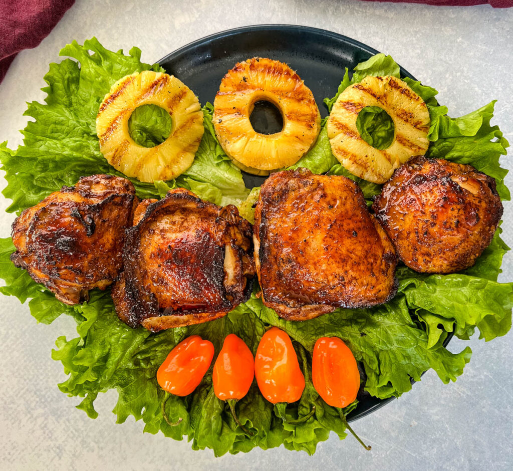 bone in Jamaican jerk chicken thighs on a plate with peppers and grilled pineapples