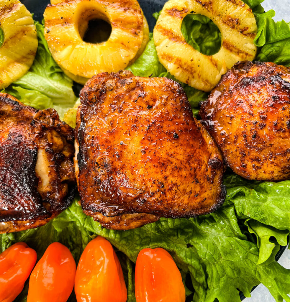 bone in Jamaican jerk chicken thighs on a plate with peppers and grilled pineapples