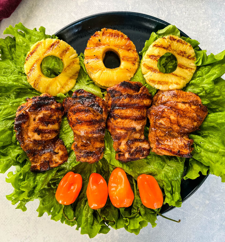 Jamaican jerk chicken thighs on a plate with peppers and grilled pineapples