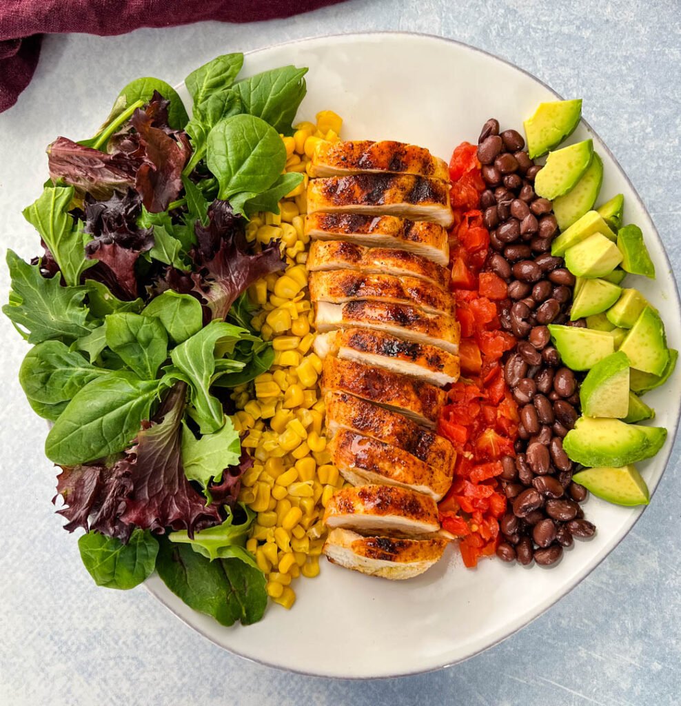 southwest salad with lettuce, corn, chicken, tomatoes, black beans, and avocado on a plate