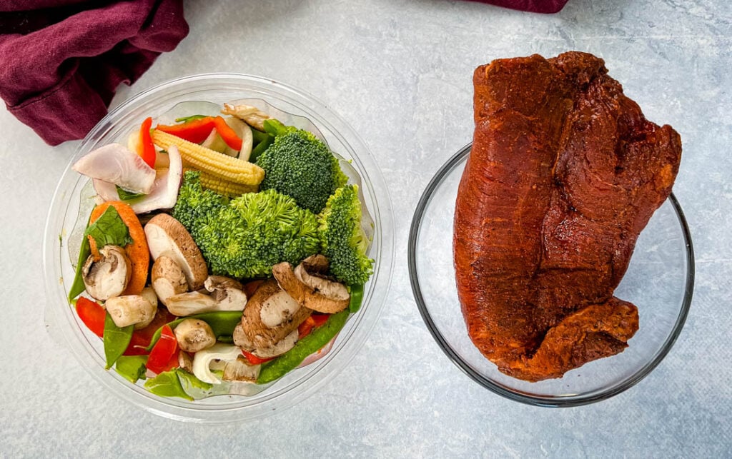 raw vegetables and raw flank steak in separate bowls