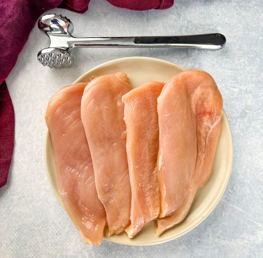 raw chicken breast cutlets on a plate with a mallet