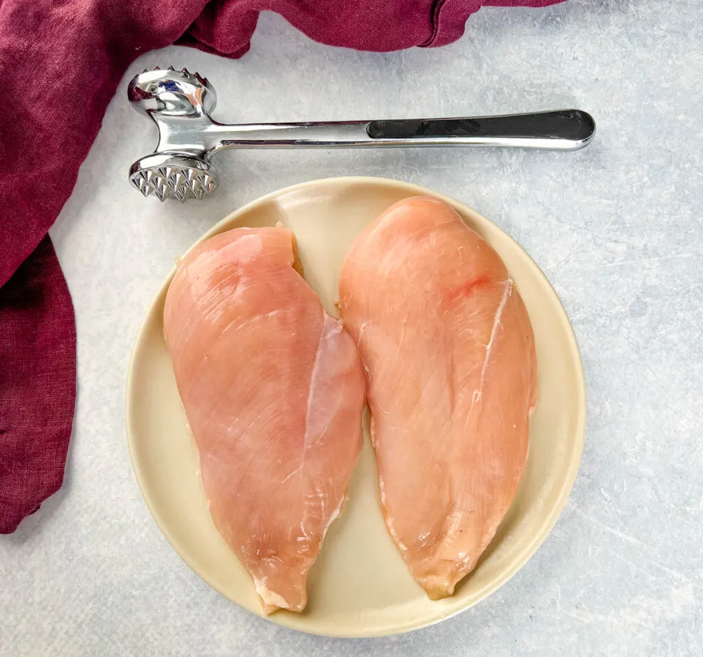 raw chicken breasts on a plate with a mallet
