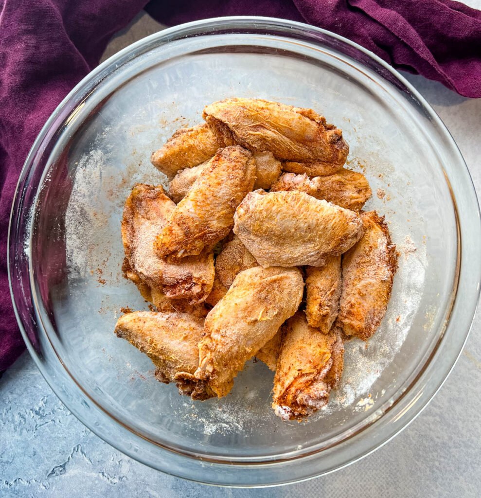 raw chicken wings with spices and flour in a glass bowl