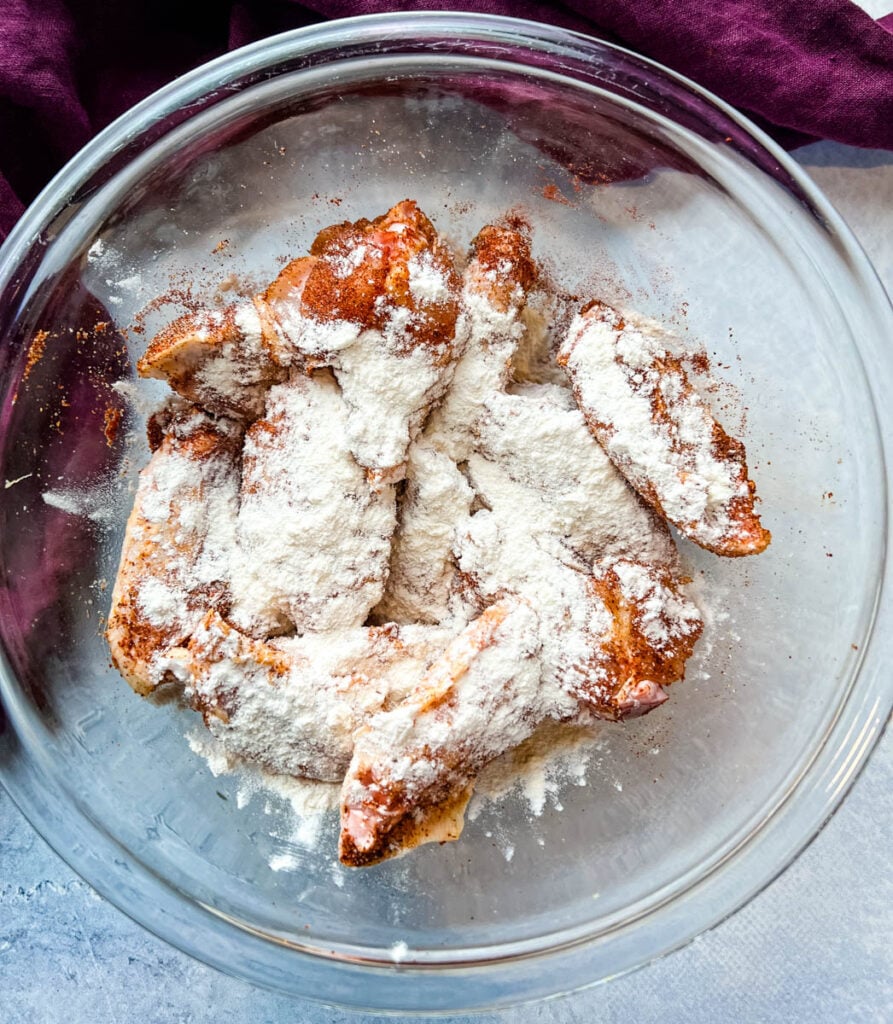 raw chicken wings with spices and flour in a glass bowl
