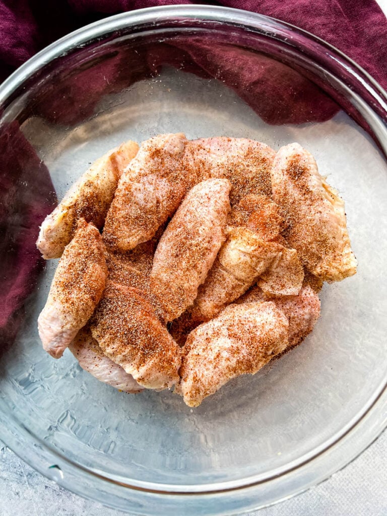 raw chicken wings with spices and flour in a glass bowl