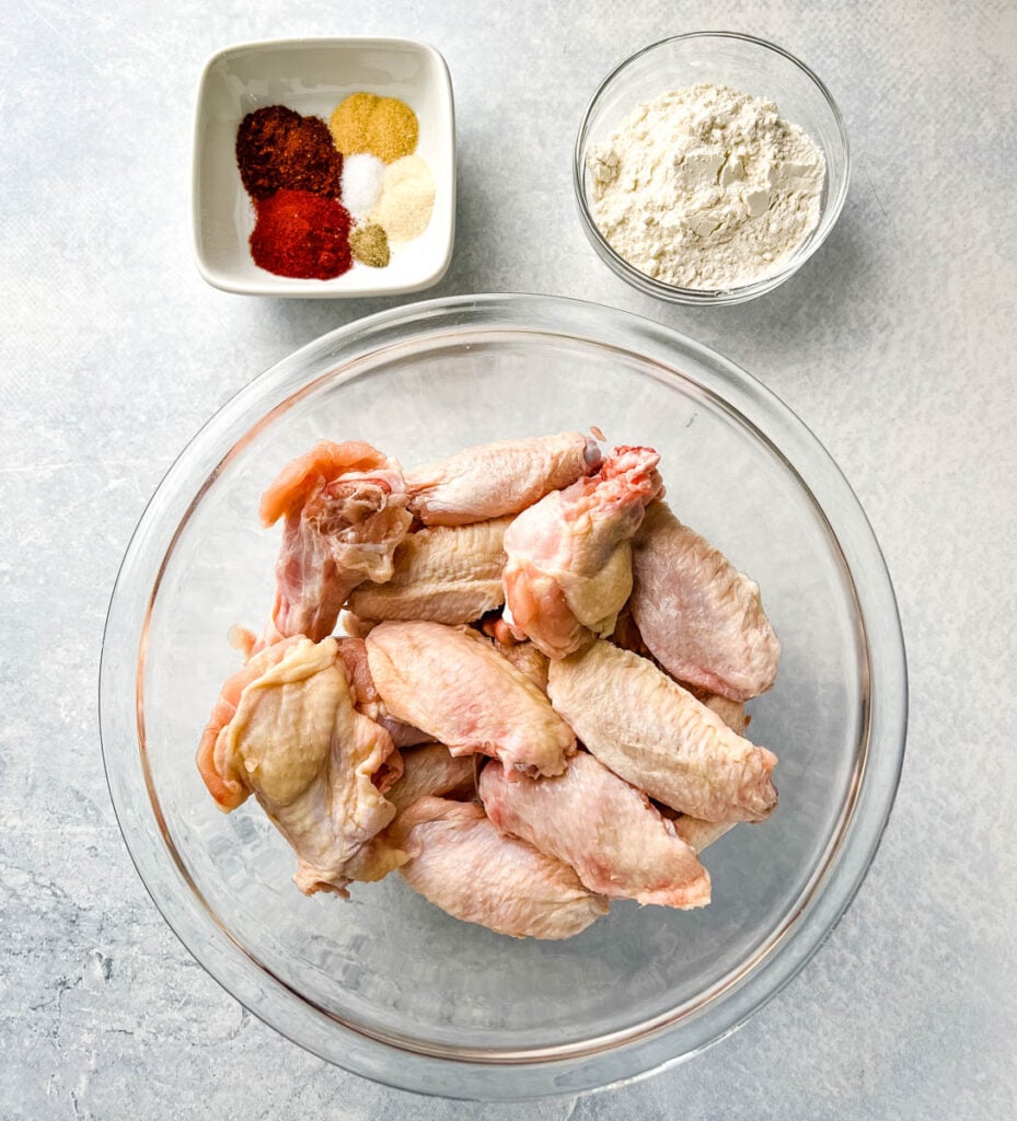 raw chicken wings, dry rub spices, and flour in separate bowls
