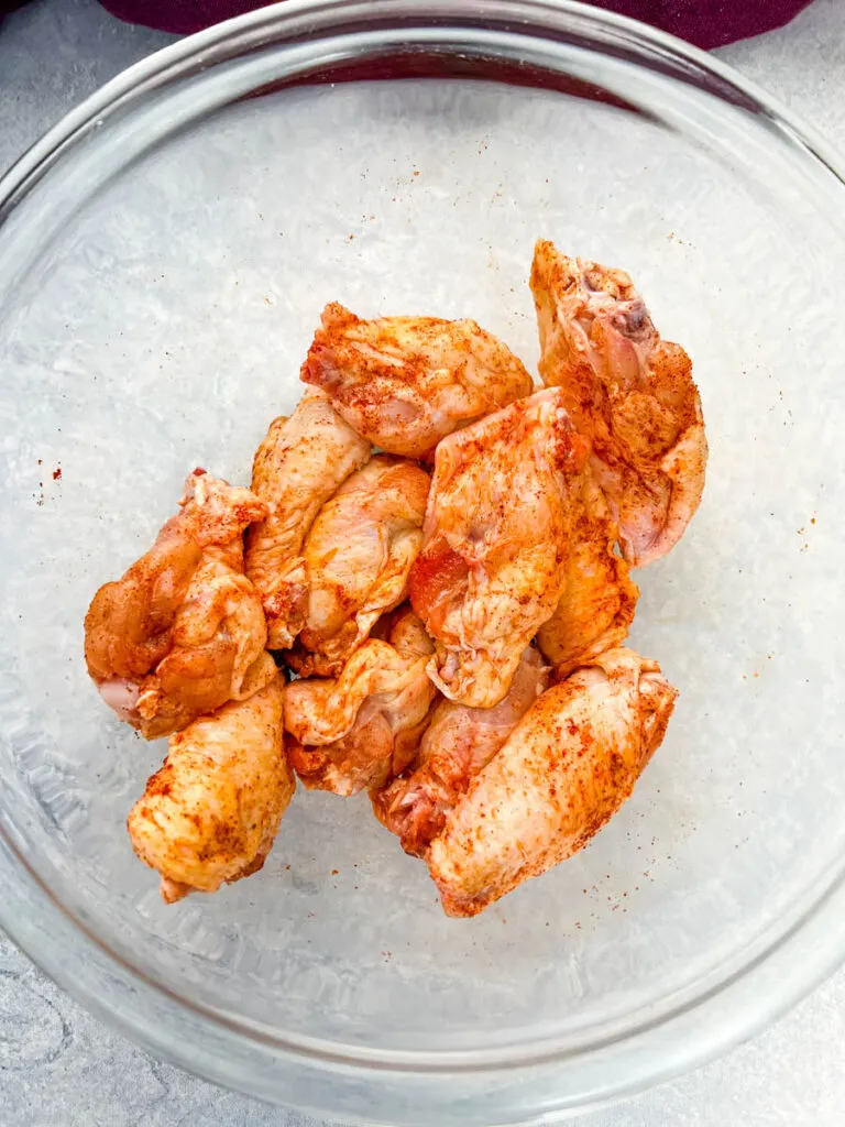 raw chicken wings in a glass bowl along with a bowl of spices