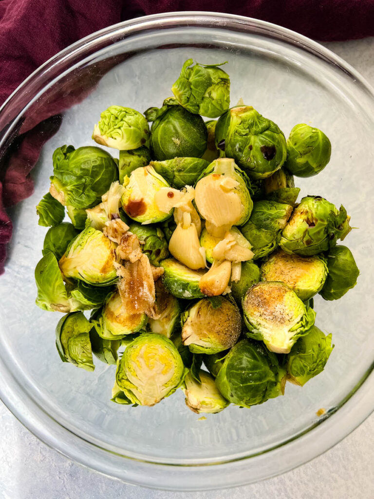 fresh, raw brussels sprouts in a glass bowl with garlic and balsamic vinegar