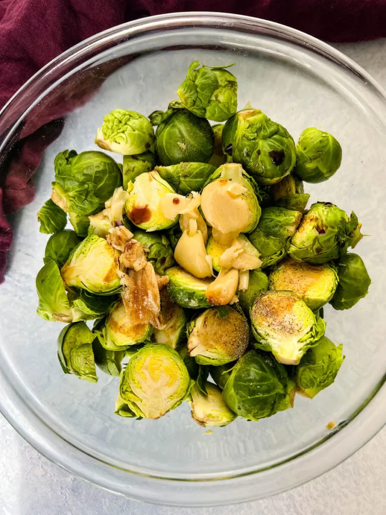 fresh, raw brussels sprouts in a glass bowl with garlic and balsamic vinegar