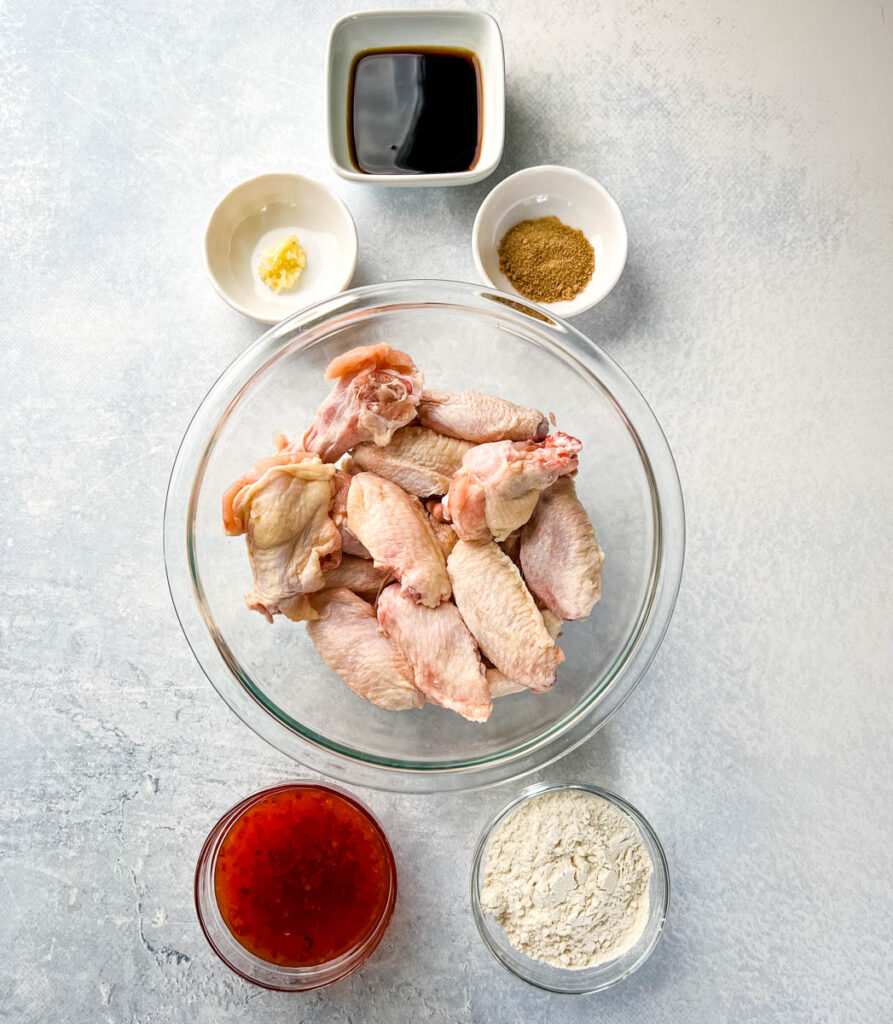 raw chicken wings, soy sauce, sweet chili sauce, garlic, flour, and spices in separate bowls