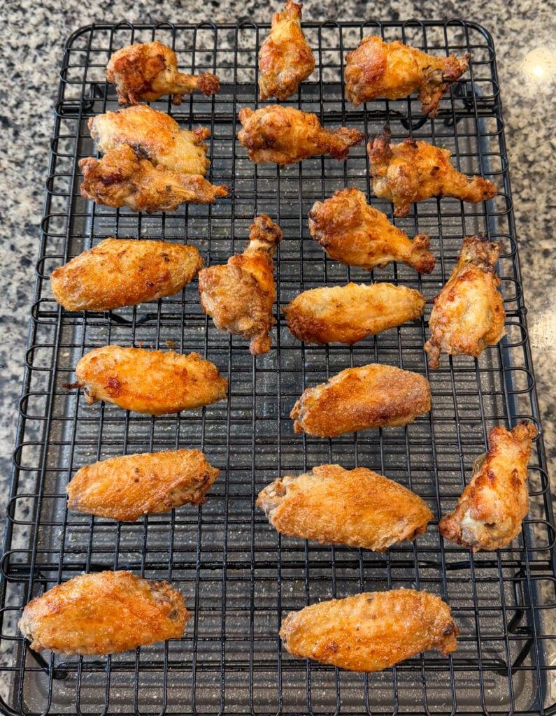 Crispy golden brown chicken wings arranged on a wire rack over a sheet pan before being coated with sweet chili sauce.