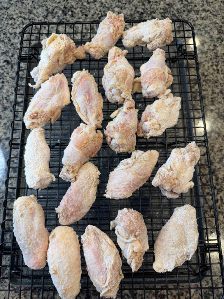 Raw chicken wings coated in seasoned flour and arranged on a wire rack over a sheet pan before cooking.