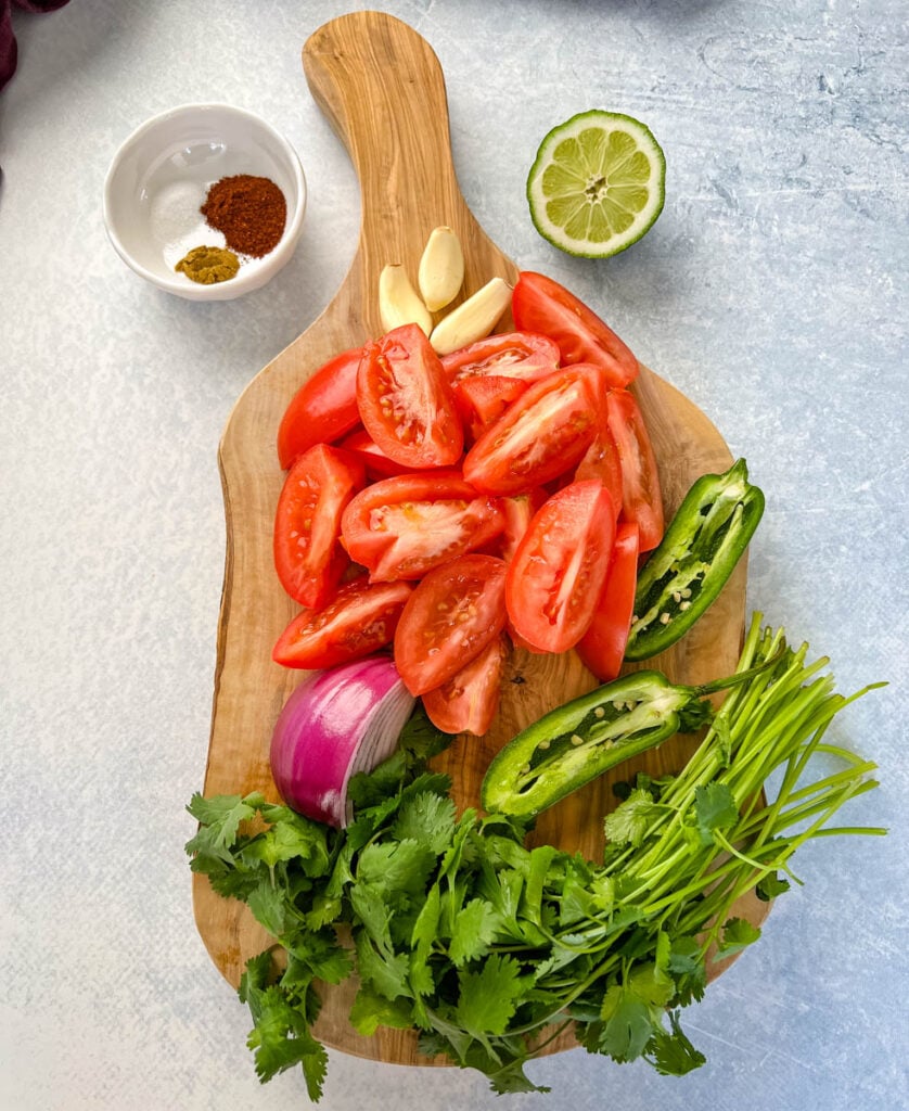 tomatoes, jalapenos, cilantro, garlic, red onion, spices, and lime on a flat surface