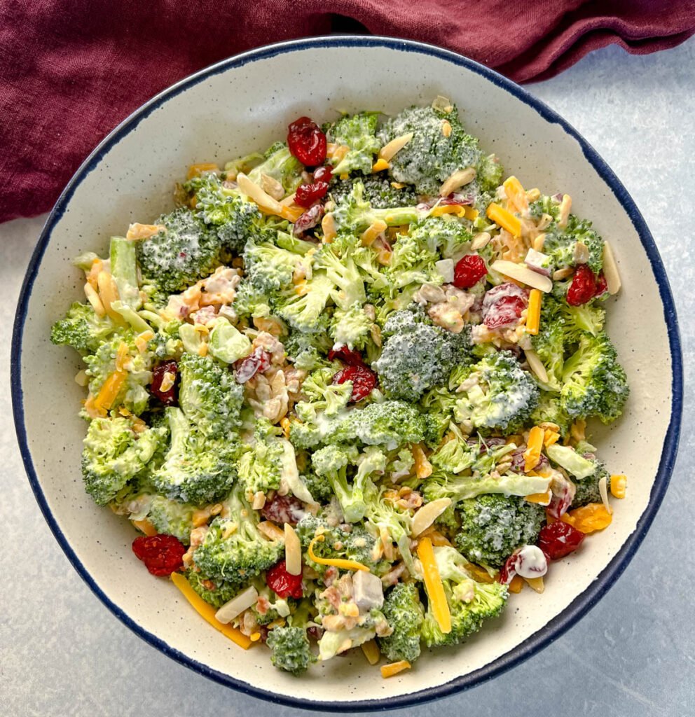 broccoli salad with cheese, bacon, and cranberries in a white bowl