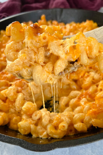 a wooden spoonful of smoked mac and cheese in a cast iron skillet
