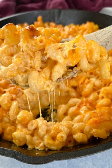 a wooden spoonful of smoked mac and cheese in a cast iron skillet