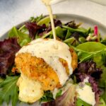 mozzarella stuffed chicken breast on a plate with salad and drizzled in cream sauce