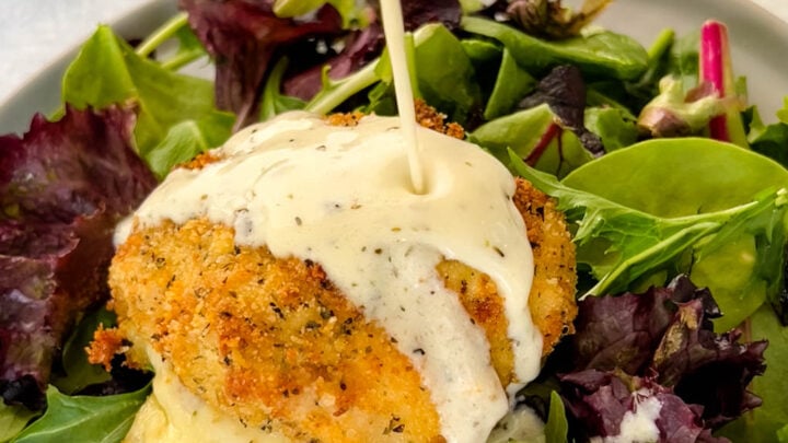 mozzarella stuffed chicken breast on a plate with salad and drizzled in cream sauce