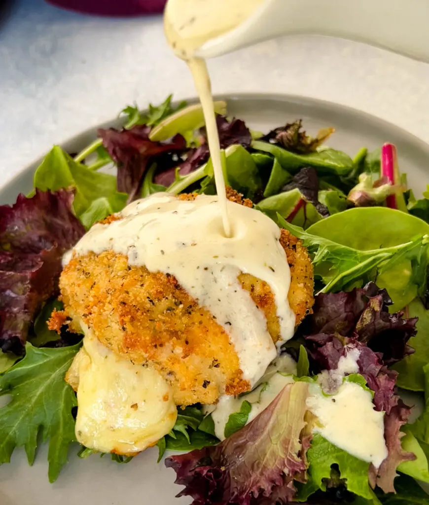 mozzarella stuffed chicken breast on a plate with salad and drizzled in cream sauce