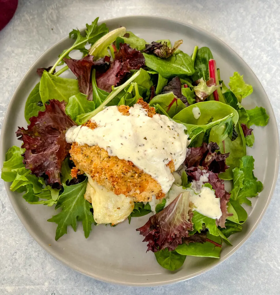 mozzarella stuffed chicken breast on a plate with salad and drizzled in cream sauce